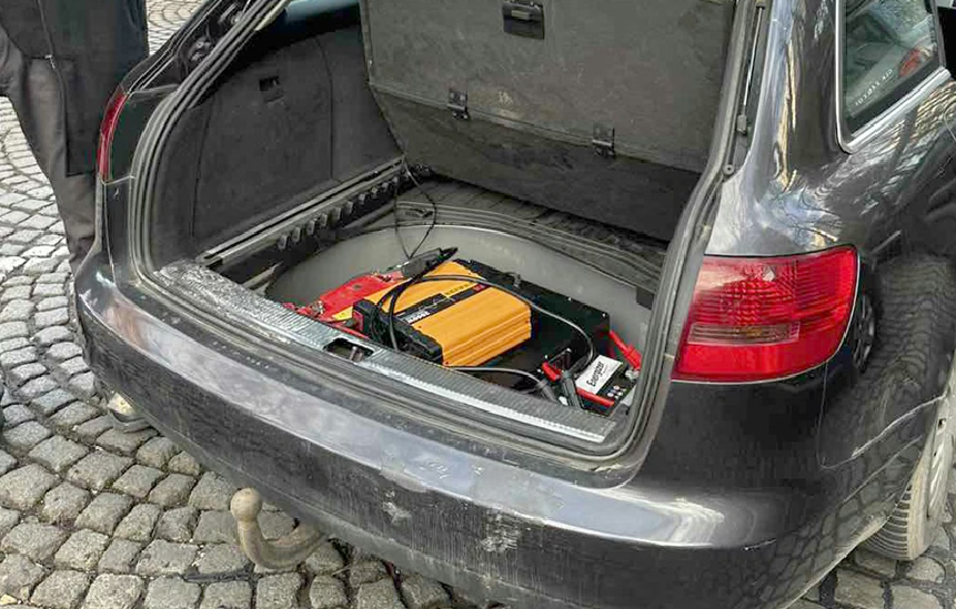 A photo with an opened trunk of a black car. SMS blaster equipment is visible in the trunk, a power unit, SIMbox, IMSI catcher, etc.). This photo was initially published on Nova.rs and belongs to Ministry of Internal Affairs, Serbia.