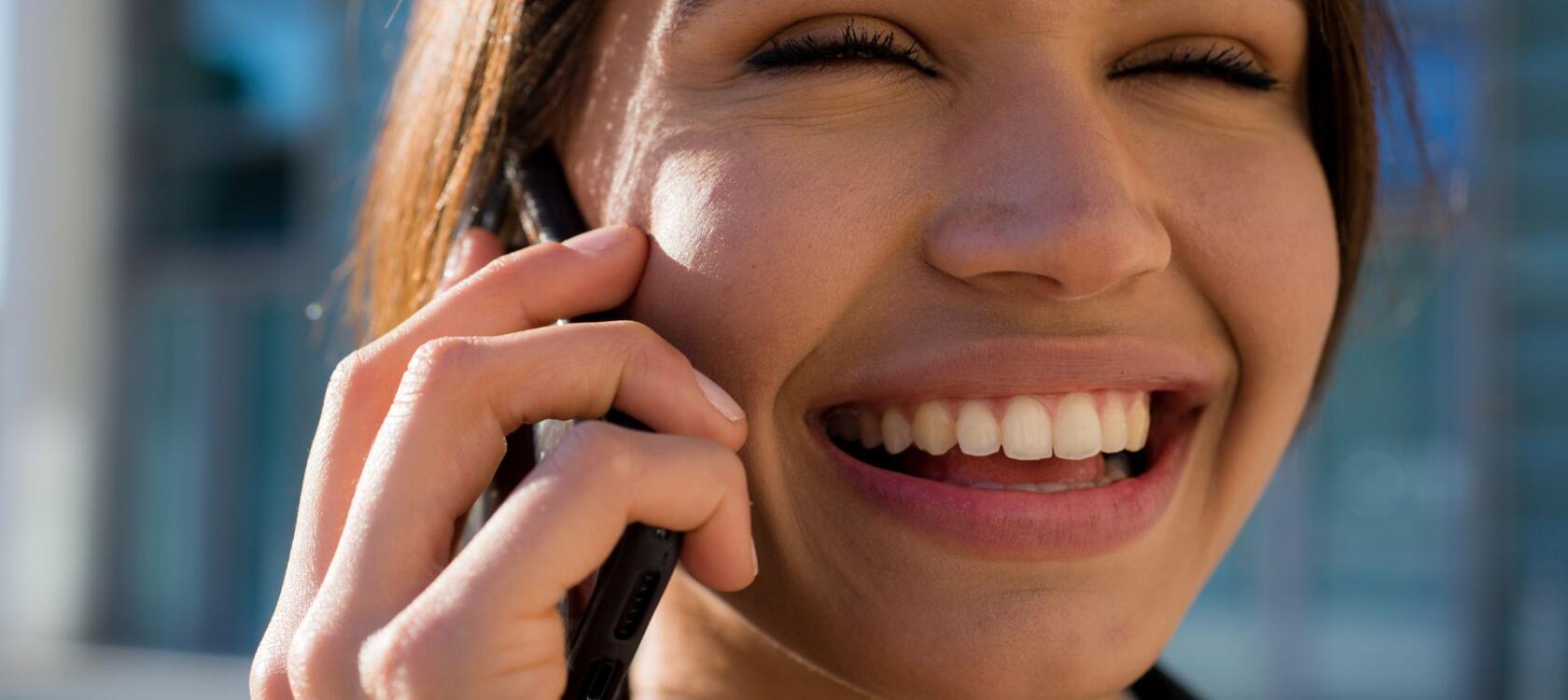 A happy woman smiling and using a cell phone for a phone call. 