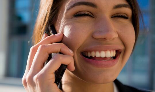 A happy woman smiling and using a cell phone for a phone call. 